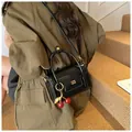 Black glossy crossbody bag with gold lettering and decorative cherry pendant detail - With Cherry Pendant Style / Black