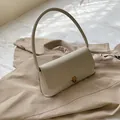 Minimalistische beige Schultertasche aus Leder mit Wildlederklappe auf einem Mantel - Weiß