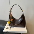 Donkerbruine glanzende hobo tas met goudkleurige gesp en kleurrijke pompon hanger - Koffie Met Hanger