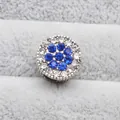 Vue macro d'un charm argenté avec motif floral en strass bleus et détails blancs - Bleu