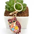 Golden owl keychain with colorful rhinestones and opal stones hanging on a plant pot - Reddish Brown Owl