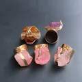 Detailansicht von fünf Rohkristallringen mit vergoldeten Hammerschlag-Ringen auf Grau - Rosa