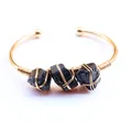 Detail van met koperdraad omwikkelde zwarte ruwe kristalstenen op gouden open armband - Zwarte Toermalijn