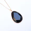 Detail eines facettierten schwarzen Tropfenanhängers mit Goldrahmen an einer feinen Kette - Obsidian