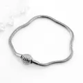 Detailed view of silver snake chain bracelet with textured cylindrical clasp on white stone - Steel Color Shell Clasp
