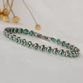 Close-up of sparkling green round zircons set in a polished silver-tone tennis bracelet - Steel Color/Green Zircon