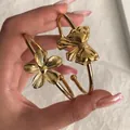 Detalle de brazaletes dorados con dijes de flor texturizada y lazo elegante - Brazalete Abierto Flor Lazo Oro (6484101HB)