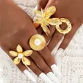 Massives goldenes Blumenring-Set mit Perlen an der Hand vor weißem Stoffhintergrund - Gold Übertriebener Großer Ring 4-Teiliges Set (6425301HB)