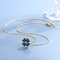 Collana a quadrifoglio dorata con cristalli a cuore blu su sfondo blu decorativo - Quadrifoglio Blu