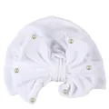 Detail of white velvet baby turban hat featuring large bow and pearl embellishments - White