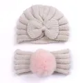 Dettaglio del cappello in maglia per neonati con fiocco e fascia con pompon rosa - Beige