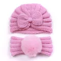 Detailed view of pink knitted baby hat with bow and matching faux fur pompom headband - Pink