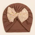 Detail of baby turban hat featuring a golden polka dot mesh bow on soft brown fabric - Coffee