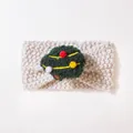 Dettaglio di fascia lavorata a maglia per neonati con trama in lana beige e pompon verde - Stile Pallina di Natale Bianco Sporco
