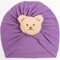 Detail einer lila Baby-Turban-Mütze mit einem weichen, beigen Plüschbären-Aufnäher - Lila