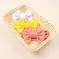 Three candy-colored baby nylon bow headbands in a woven basket with soft fabric texture - White, Bright Yellow, Dusty Rose