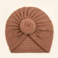 Close-up of waffle knit texture and central knot detail on this camel baby donut hat - Coffee
