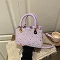Bolso de mano morado claro a la moda con tachuelas de estrellas y asa tejida en una mesa - Púrpura