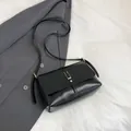 Detail view of black faux leather shoulder bag featuring gold U-shaped buckle and fine strap - Black