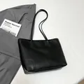 Detail of black lychee grain leather tote bag with reinforced stitching on gray blazer - Black
