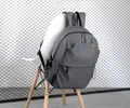 Close-up of a matte grey waterproof backpack hanging on a modern chair with metal mesh - Gray