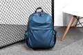 Detail of navy blue water-resistant backpack showing front zip pocket and side bottle pouch - Blue