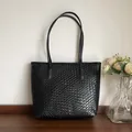 Detalle del bolso de mano trenzado negro de cuero sintético sobre una mesa de madera - Negro