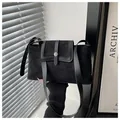 Detail shot of black minimalist handbag showing matte texture and metal snap closure - Black