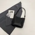 Sac seau minimaliste en cuir noir avec bandoulière à nœud et détails dorés - Surface en Cuir Lisse / Noir PU