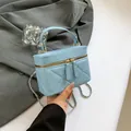 Light blue quilted mini bucket bag with gold chain strap and top handle held by hand - Blue