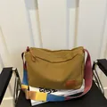 Sac bandoulière en toile moutarde avec sangle rayée posé sur une chaise en cuir noir - Marron