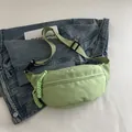 Light green nylon waist bag with adjustable strap and decorative zipper on denim background - Green