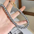 Macro detail of round grey pearls necklace featuring a minimalist gold geometric clasp - Gray