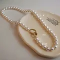 Detail of round white pearls with a unique gold irregular metal clasp on a ceramic plate - White