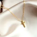 Macro shot of minimalist gold cross pendant on a fine O-chain over white satin - Gold