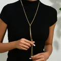 Detail of a golden Y-shaped snake bone tassel necklace worn on a black sweater - Gold Long