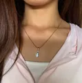 Detail of a gold teardrop necklace with blue gemstone on model wearing a pink jacket - Titanium Steel Necklace / Blue Water Drop (Gold)