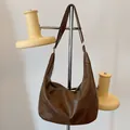Minimalist large crescent shoulder bag in deep brown soft leather hanging on a stand - Brown
