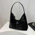 Detail of glossy black velvet hobo bag featuring smooth leather shoulder strap and oval patch - Black