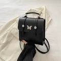 Mochila pequeña negra de cuero con hebilla de mariposa dorada y asa superior estable - Negro