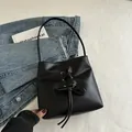 Bolso cubo negro minimalista con detalle de lazo sobre fondo de mezclilla texturizada - Negro