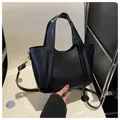 Detalle del bolso trapezoidal de cuero PU negro con herrajes dorados sobre una silla - Negro
