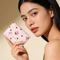 Pink trifold wallet with cherry bow print and brand label held by a model - Pink