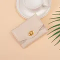 Elegant beige tri-fold wallet with gold ring twist lock and subtle glitter side panels - White