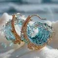 Golden ocean wave hoop earrings with blue resin and crystals on a white sand beach - Gold Earrings