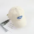 Top-down view of cream cotton baseball cap with blue embroidered letter patch and air holes - Circumference 48-52cm / Beige