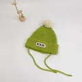 Detail of green knit baby hat with white pom-pom, letter patch and side straps - S (48-52cm) / Yellow-Green