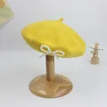 Detailansicht der gelben Wollbaskenmütze mit weißer Perlen-Schleife als Dekoration - S Kinder (49-52cm) / Gelb
