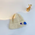 Cream knit beanie for children featuring a bright blue smiley face safety pin detail - S (48-53cm) / Beige (Blue Pin)