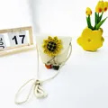 Detail der geflochtenen Kinder-Strohtasche mit gelber Sonnenblume und bunten Anhängern - Kürbis & Sonnenblume / Creme